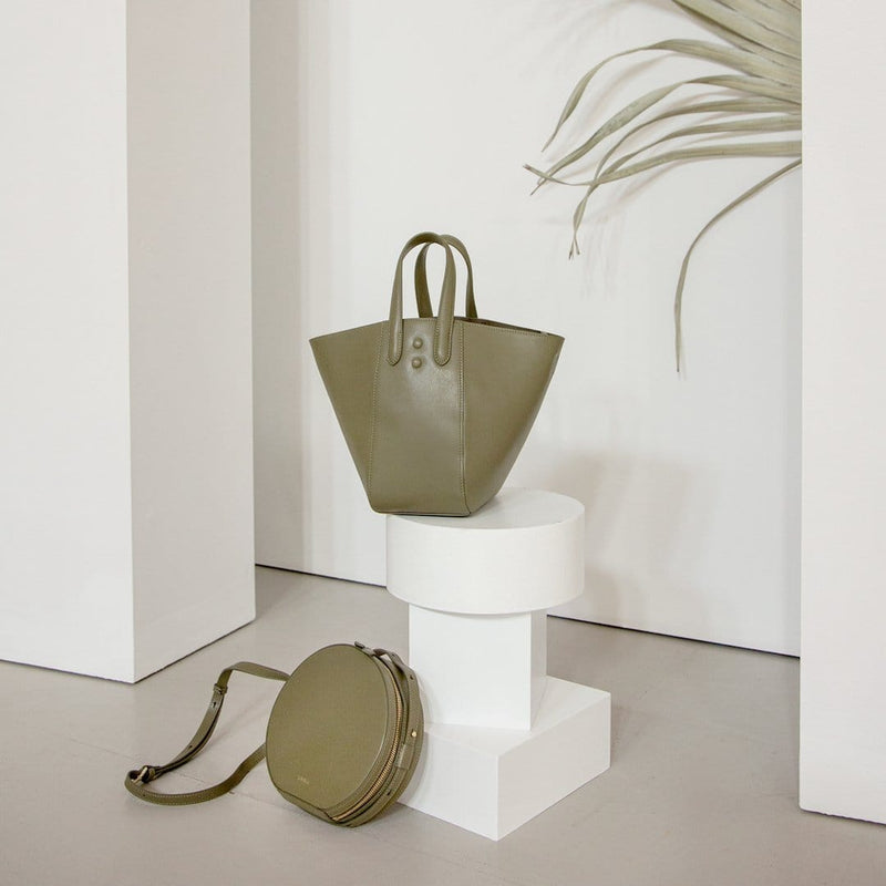 Khaki hybrid bucket tote bag and round Khaki shoulder bag pictured next to white sculture, luxury genuine leather bags, gold hardware.
