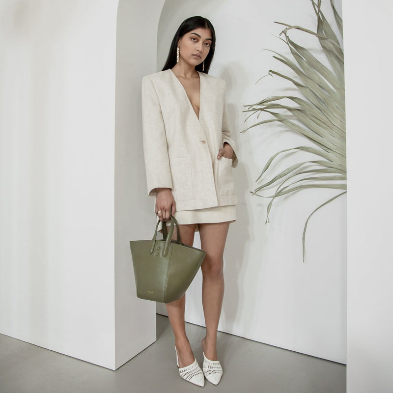 Woman pictured near to a green palm with khaki leather handbag, luxury tote bucket hybrid bag.