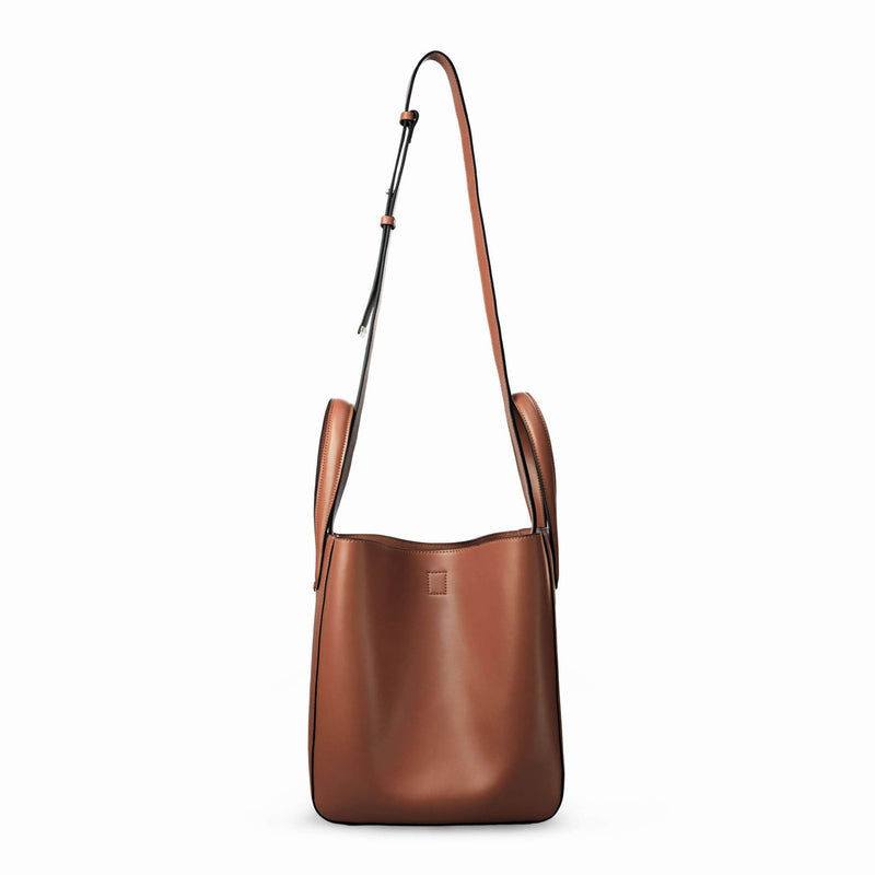 Side view of X NIHILO Eight in tan bag, fashion bag with single snap button top closure, soft gold hardware, and adjustable shoulder straps, luxury cow nappa leather handbag, genuine leather bag with strap at full length.