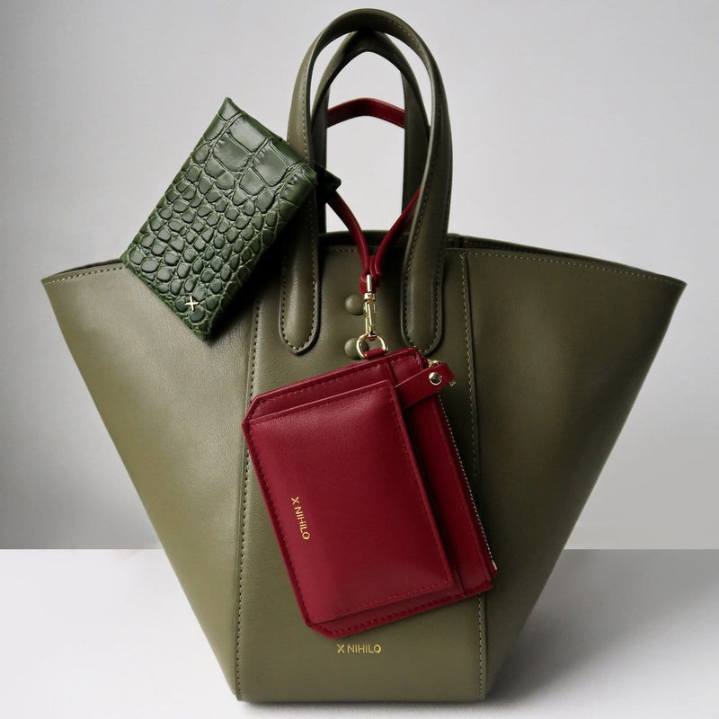 Olive croc print cardholder and small red leather wallet and coin purse placed on an avocado green trapezoid leather handbag, luxury leather goods.