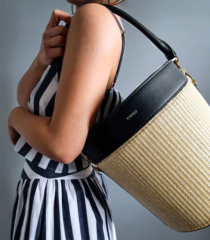 Model carrying the raffia picnic basket with black leather top on the side and detachable leather handle, on her shoulder.