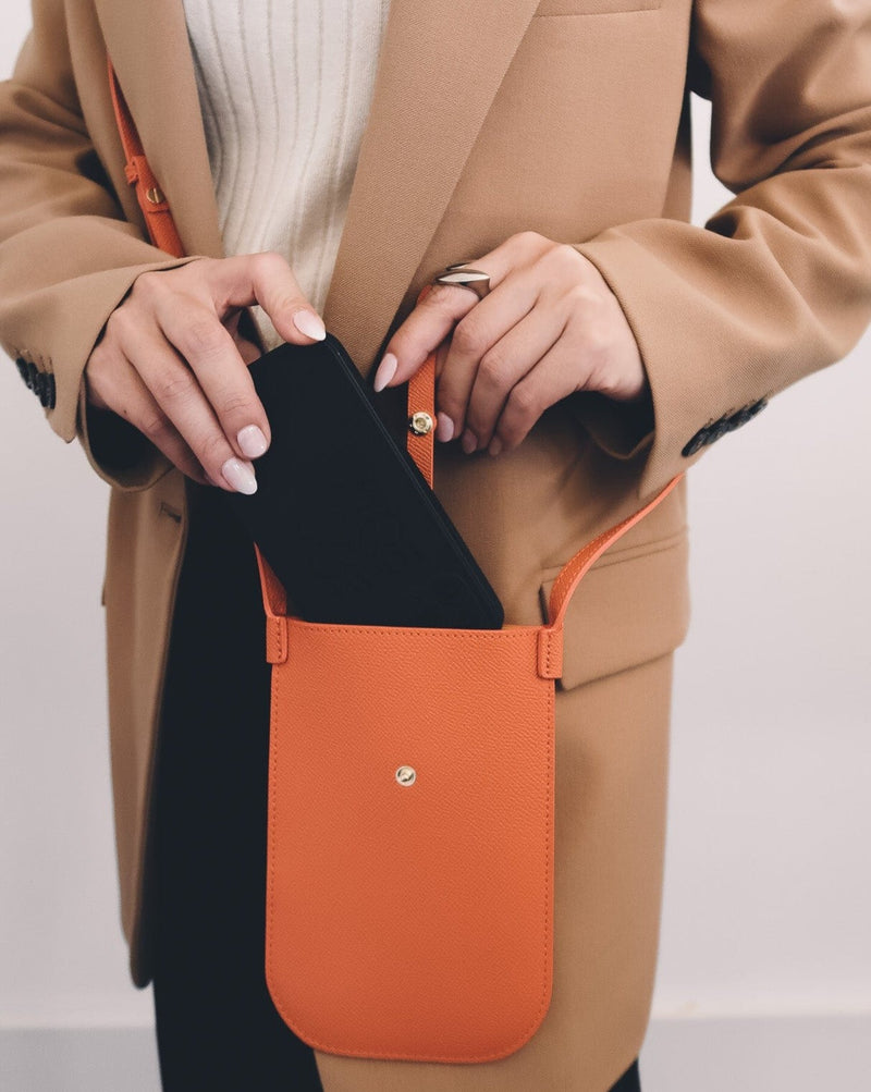 Model wearing rectangular Tangerine orange phone pouch with opening on top and an attached shoulder strap.