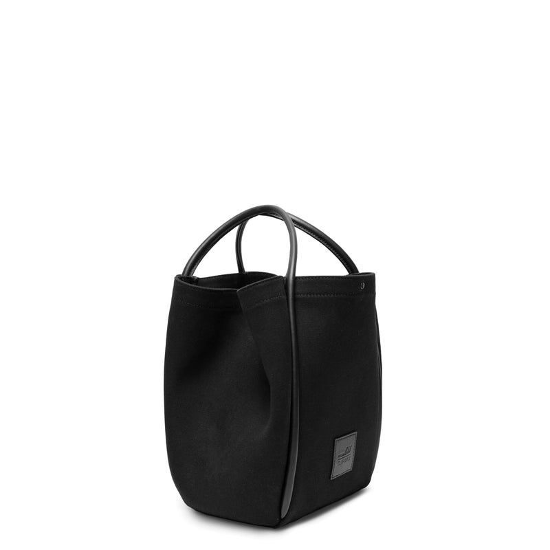  Side view of black canvas tote bucket bag, with black leather rolled leather handles, silver button closure at the top and small square logo of WEST14TH and X NIHILO. Shown as bucket bag, with button used to bring in wings.