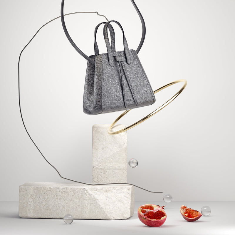 3D detailed artistic composition of mini gunmetal bucket shape bag with leather pull-strings, a gold ring and a pomegranate