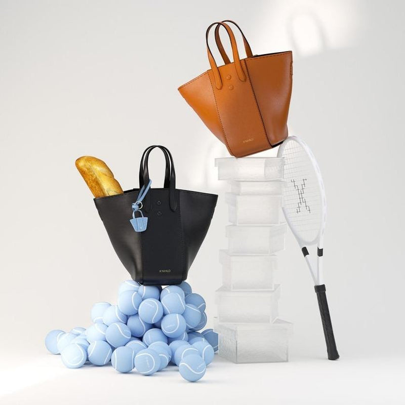 3D animation of two large genuine leather tote bucket bag hybrids, one in tan and the other in black, shown with tennis balls and a tennis racket.