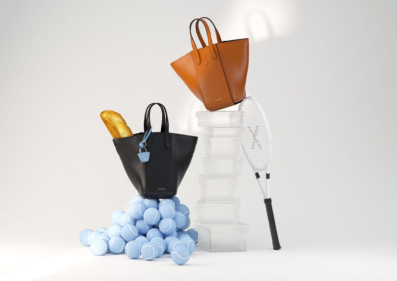 3D animation of two large genuine leather tote bucket bag hybrids, one in tan and the other in black, shown with tennis balls and a tennis racket.