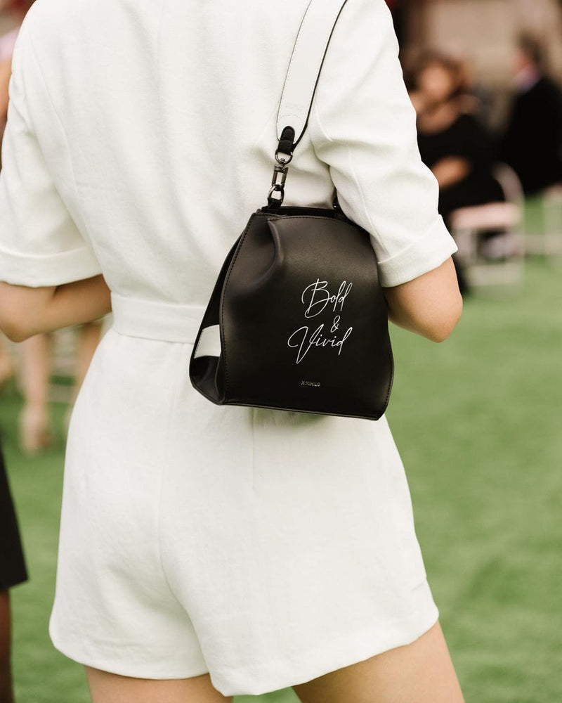 Woman wearing Black luxury leather bag over her shoulder using genuine nappa leather black and white bag strap with silver hardware and X NIHILO logo embossed in silver near clasp.
