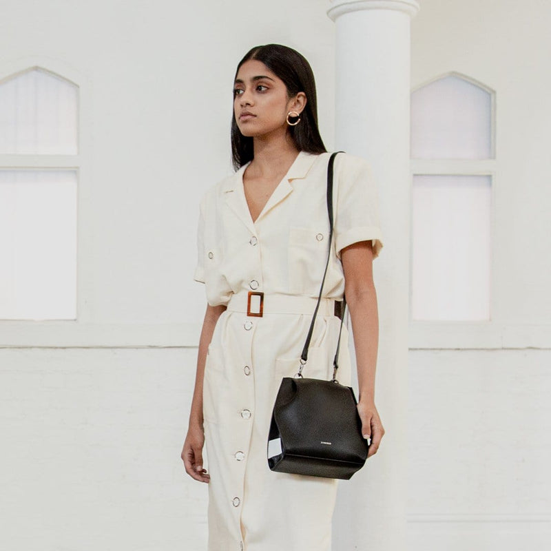 A woman wearing all white with the black and white stripe leather hybrid mini bucket bag on one shoulder, standing against a white background.