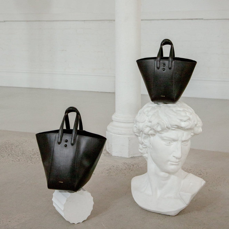 White roman head sculpture pictured with two black genuine nappa leather handbags, luxury bucket tote hybrids.