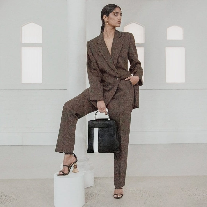Woman in brown suit holding X NIHILO Hunter in black and white stripe backpack bag, fashion bag with high shine gunmetal hardware, detachable and adjustable strap, two hidden magnetic clasps closure for front compartment, pockets fitted inside, and zip closure for back compartment, luxury cow nappa leather handbag, genuine leather bag