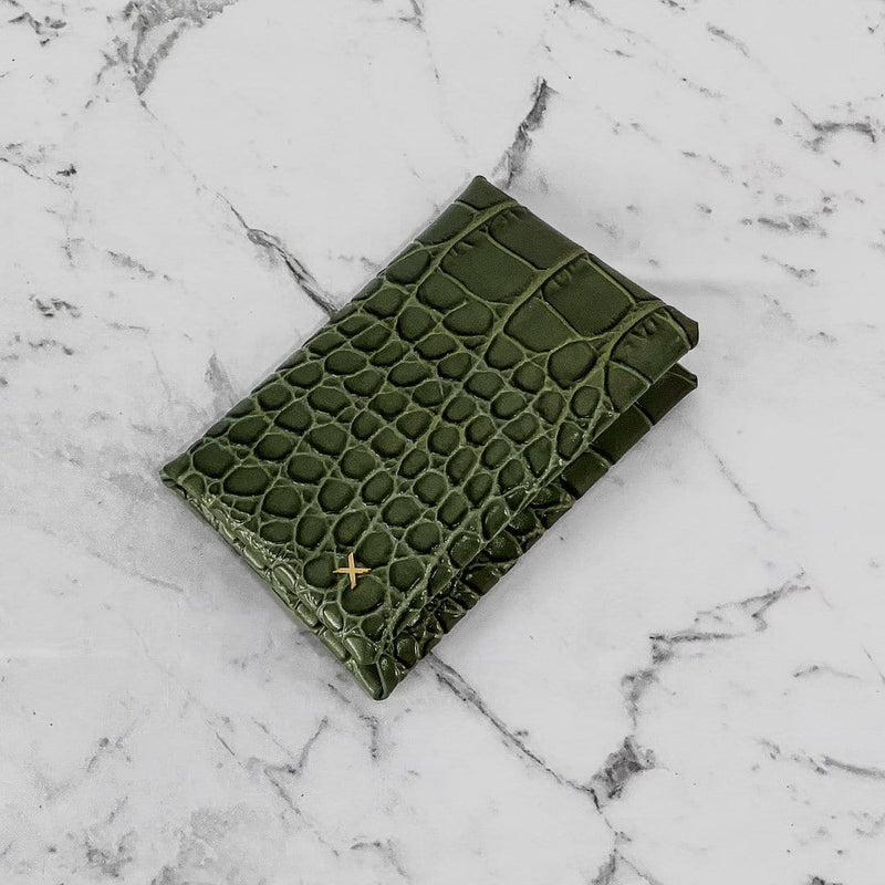 Olive croc print leather cardholder with logo X in gold hardware in the bottom corner of the cardholder, placed on a white marble background.