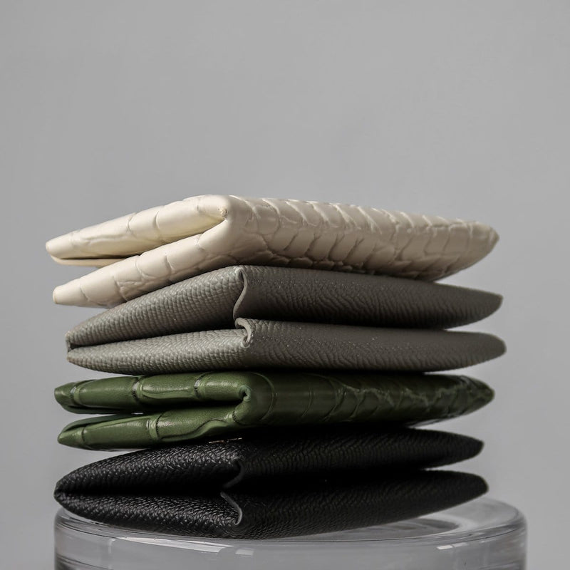 Four textured leather cardholders stacked on top of one another, the colours are black, green, grey and white in the order from bottom to top.