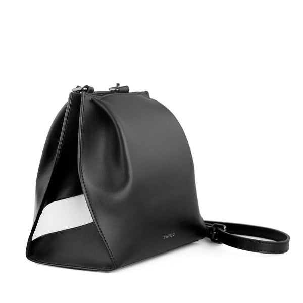 Angled side view of hybrid mini bucket bag in black with white stripe,  genuine nappa leather, with gunmetal hardware, detachable and adjustable strap, two press-stud on sides of the top opening.