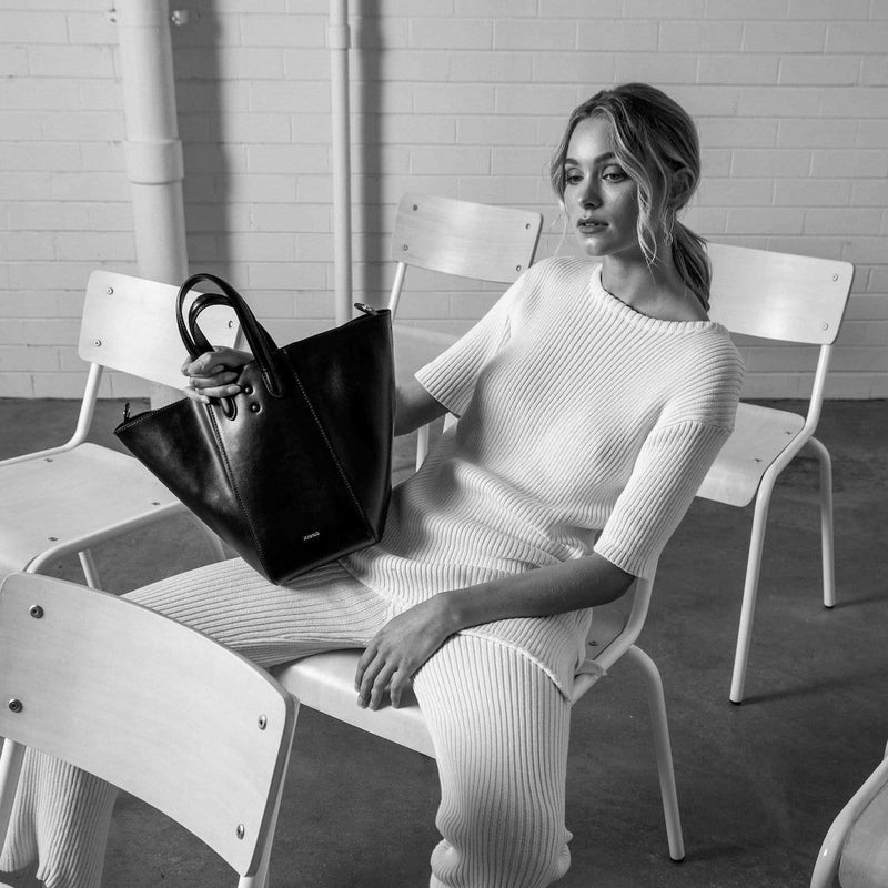 Woman on a chair holding a black genuine nappa leather handbags, bucket tote hybrid.