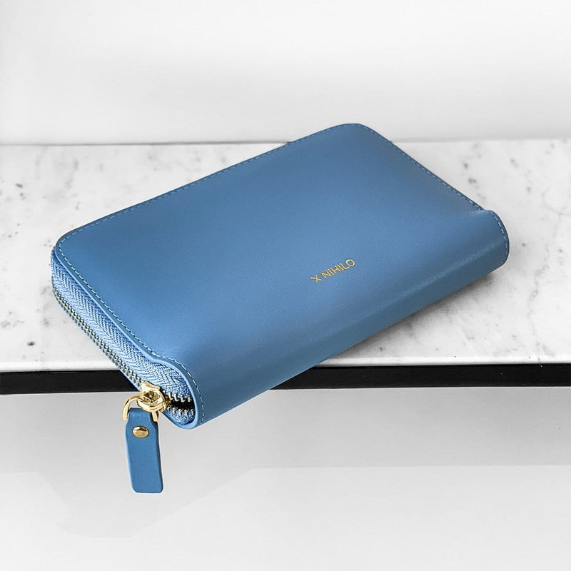 Sky blue leather wallet and passport holder placed on an angle with logo X NIHILO embossed on the surface.