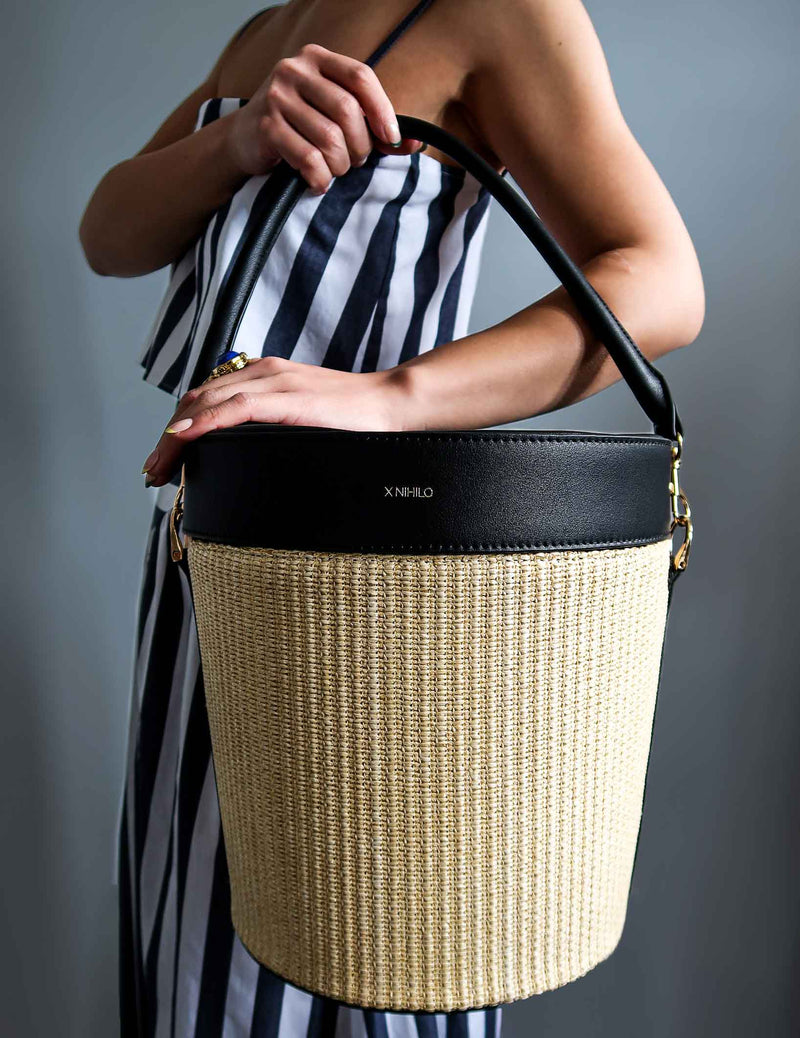 Model carrying the raffia picnic basket with black leather top on the side and detachable leather handle as a handbag.