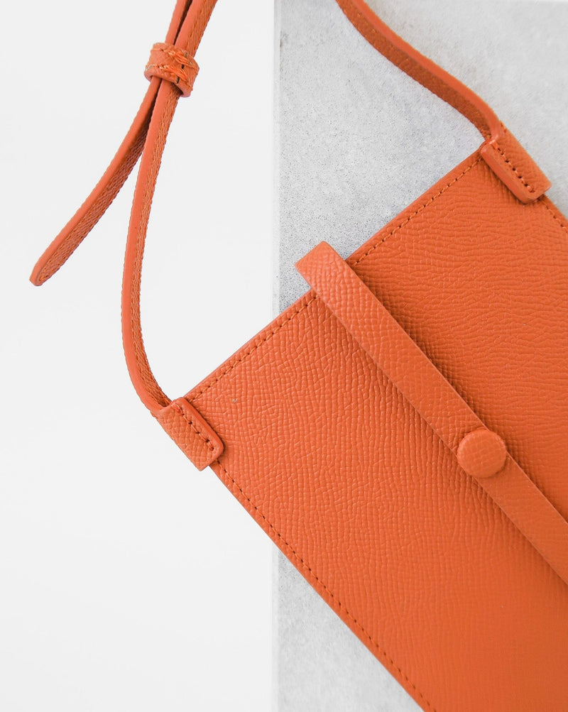 Close up of Rectangular Tangerine orange phone pouch with opening on top and an attached shoulder strap.