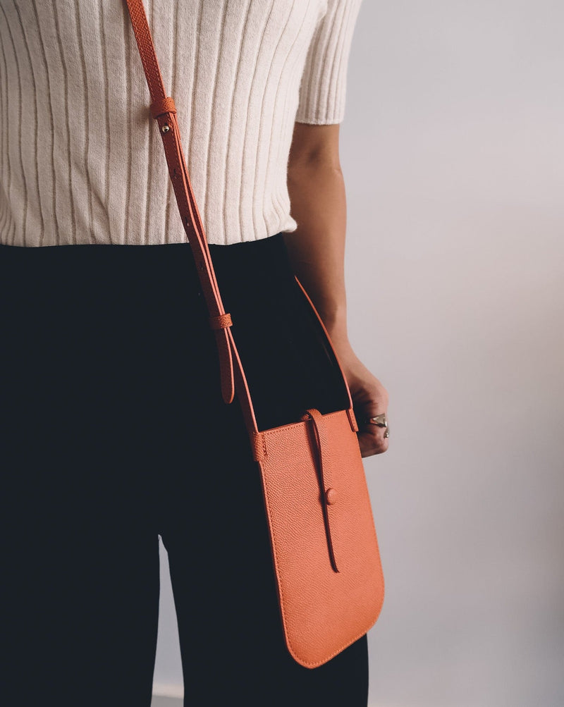 Model wearing rectangular Tangerine orange phone pouch with opening on top and an attached shoulder strap.