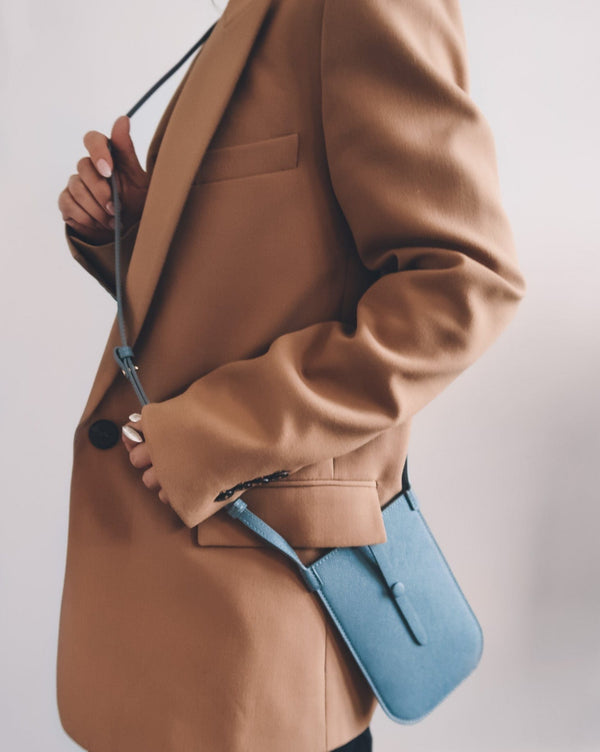 Model wearing rectangular Chambray blue phone pouch with opening on top and a attached shoulder strap.