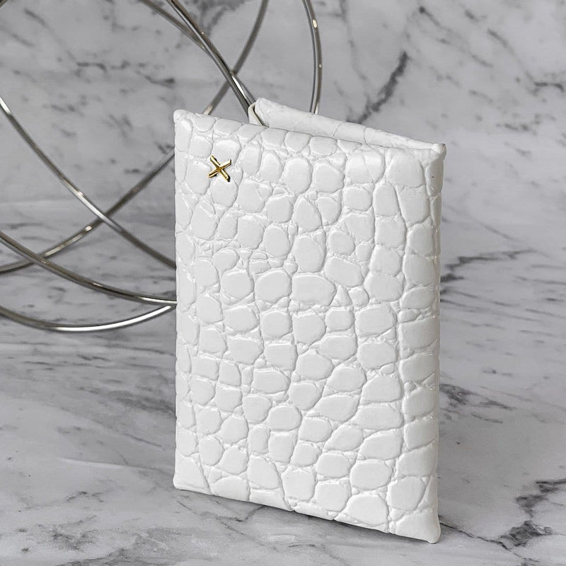 White croc print leather cardholder with logo X protruding in gold on the surface, placed with a white and grey marble background.