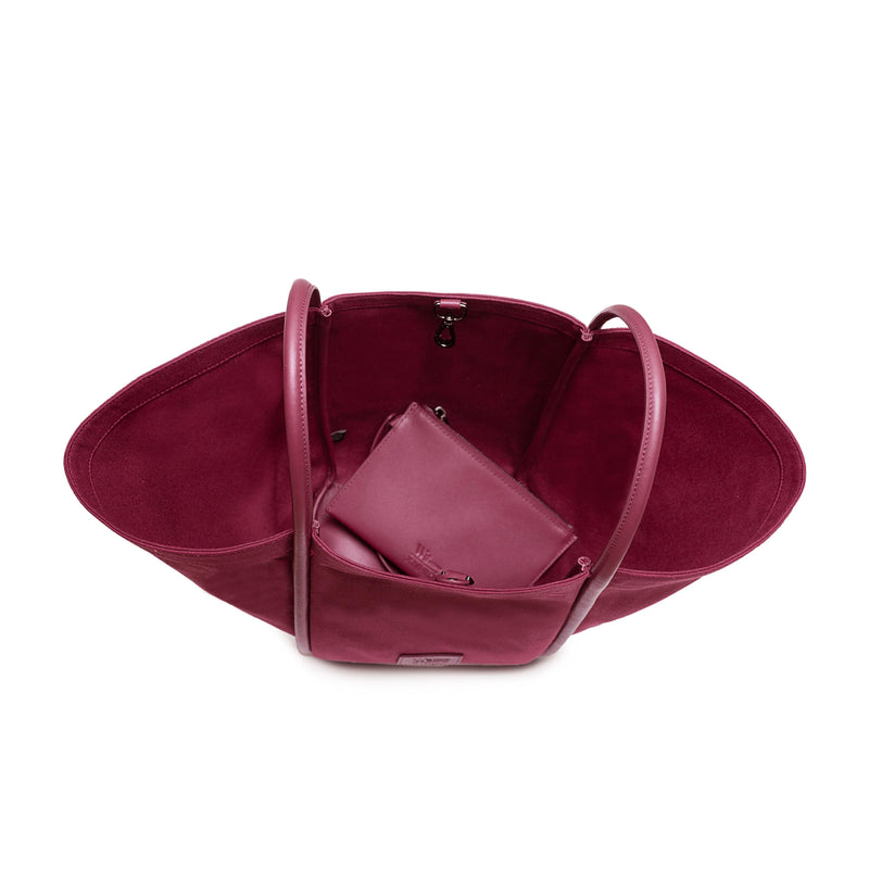Top inside view of burgundy canvas tote bucket bag, with burgundy rolled leather handles, silver button closure at the top and small square logo of WEST14TH and X NIHILO on the bottom front. Shown with included small burgundy leather pouch on the inside.