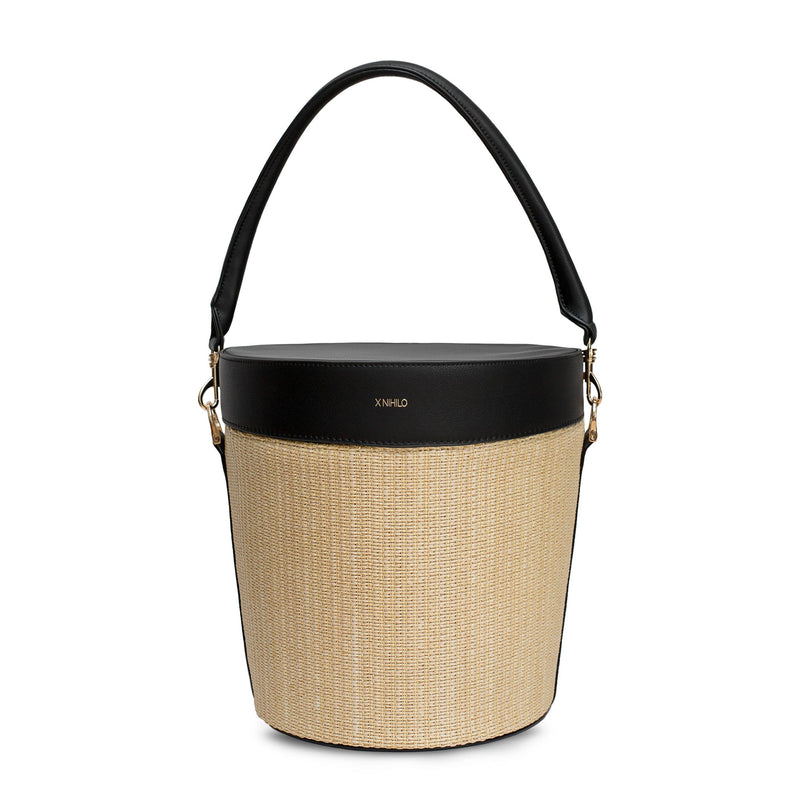 Open raffia picnic basket with black leather top on the side and detachable leather handle on the back. Gold logo embossed on the top with soft gold hardware on the sides. Front view