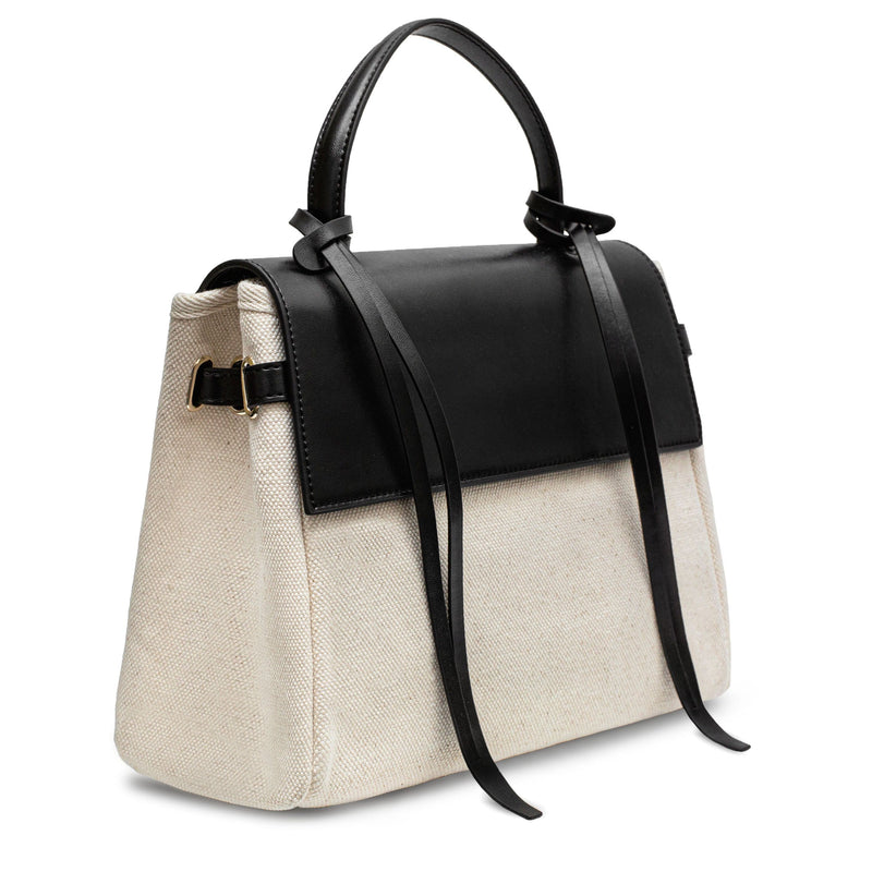 Angled side view of Black cow nappa leather and natural canvas fabric trapezoid bag with black leather tassels, front flap and handle, work bag, fashion bag