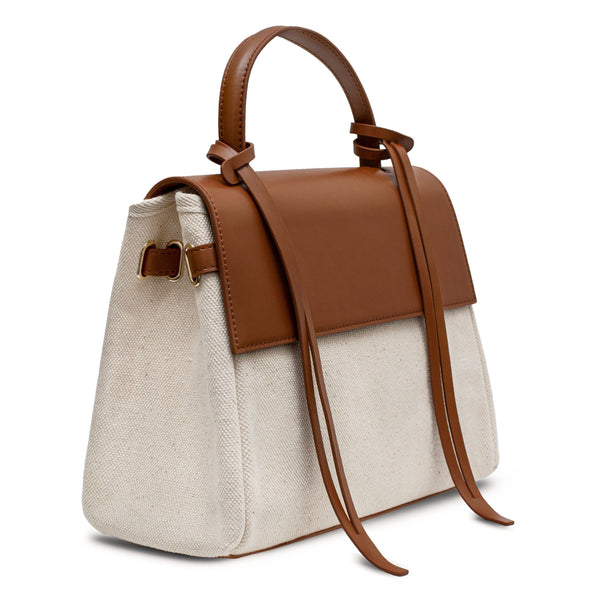 Angled side view of tan cow nappa leather and natural canvas fabric trapezoid bag with tan leather tassels, front flap and handle.
