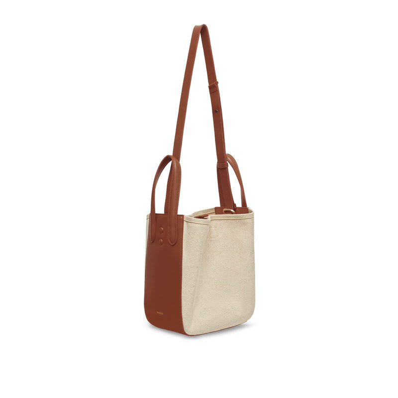Side view of tan leather and natural canvas tote bucket bag, genuine nappa leather bag with handle and logo X NIIHILO embossed in gold on the bottom front with strap at full length.
