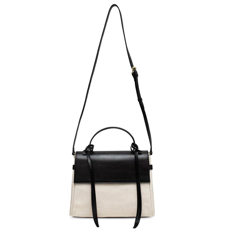 Black cow nappa leather and natural canvas fabric trapezoid bag with black leather tassels, front flap and handle, its black strap extended fully  upward.
